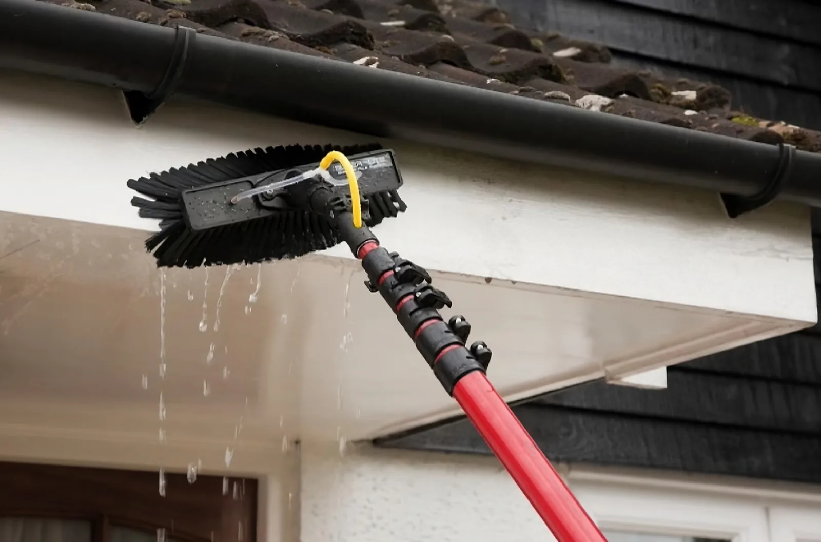 A brush head cleaning a white soffit, water running off